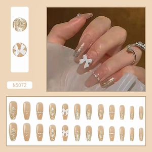 Detail of nude pink press-on nails with golden glitter gradient and white 3D bows