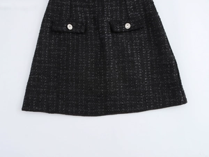 Detail eines schwarzen Tweed-Kleides in A-Linie mit Ziertaschen und Rundknöpfen