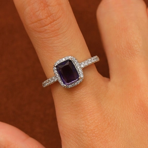 Macro shot of silver ring with rectangle purple gemstone and halo zircon crystals