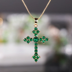 Detailed close-up of golden cross pendant featuring brilliant green circular zircon stones