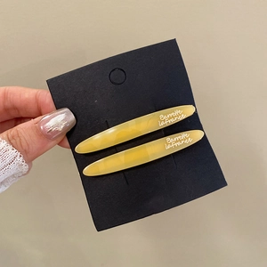 Detail of two yellow resin hair clips with French lettering on black backing card