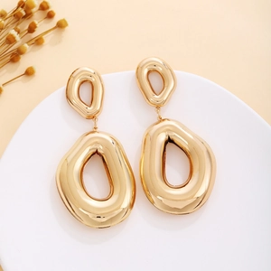 Detailed close-up of golden abstract geometric hollow earrings on white ceramic tray