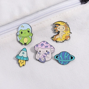 Detail of five cartoon enamel pins featuring space frog, axolotl, and mushroom on canvas