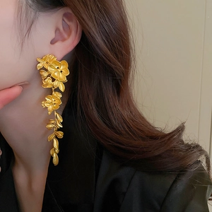 Close-up of long gold flower leaf tassel earrings worn by a model in a side view