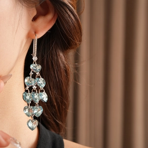 Close-up of long tassel earrings featuring blue heart crystals on a model with warm lighting