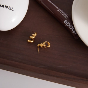 Détail de boucles d'oreilles spirales en acier plaqué or 18K sur plateau bois