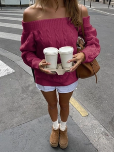 Detail of burgundy off-shoulder knit sweater with cable pattern in urban street setting