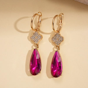 Detail of elegant gold earrings with rose red pear-shaped crystal and clover accents