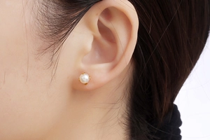 Close-up of elegant mini pearl stud earring in gold plating on a model's ear