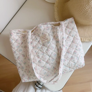 Detail view of pink floral quilted cotton tote bag on white surface with straw hat