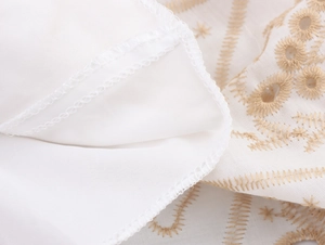 Detailed close-up of beige embroidery and fine stitching on white breathable fabric