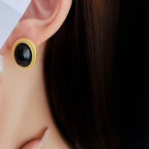 Close-up of vintage oval black stone earrings with gold metal frame worn by a model