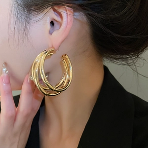 Close-up of model wearing gold layered hoop earrings with a triple-ring textured design