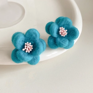 Détail de boucles d'oreilles fleurs en feutre bleu avec perles roses sur plateau
