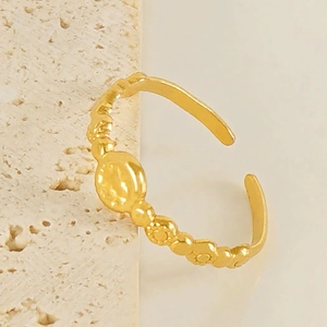 Bague ouverte dorée avec texture fleurs et perles sur support en pierre beige