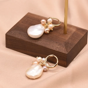 Golden baroque pearl earrings featuring small pink and white pearls on a display stand