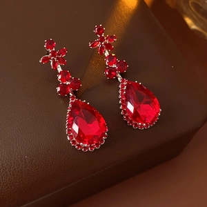 Macro shot of vintage zircon flower and red teardrop pendant earrings on leather
