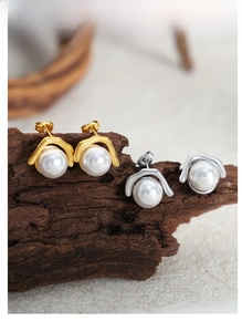 Detail of gold and silver plated titanium steel earrings with white pearls on wood
