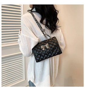 Black quilted shoulder bag with silver bow detail and leather chain strap on model