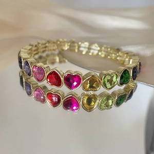 Macro shot of colorful heart-shaped gems on a gold bracelet over silk and mirror
