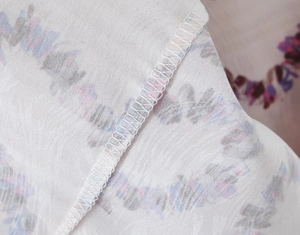 Close-up of floral print fabric detail and white overlock stitching on a slim dress