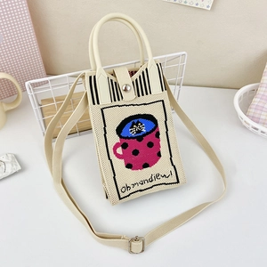 Detail view of cream knitted crossbody bag featuring a cartoon cat design and soft texture