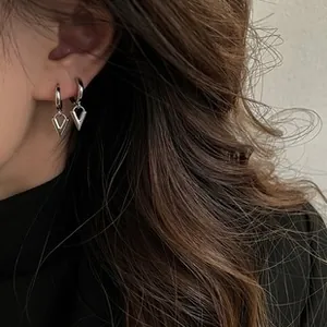 Close-up of silver irregular V-shaped pendant hoop earrings worn on a model's ear