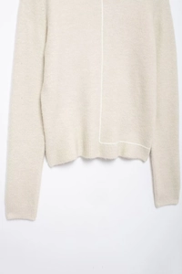 Detail of beige knit sweater showing asymmetric white stitching and soft ribbed cuffs