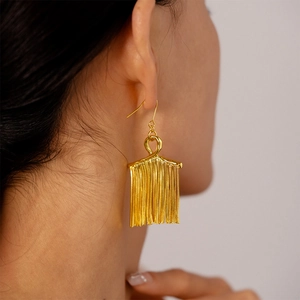 Detailed close-up of a model wearing long golden metallic tassel earrings with high shine