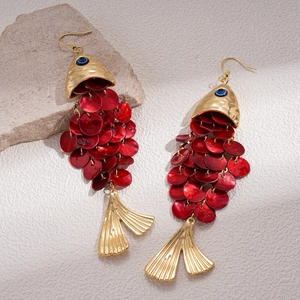 Macro shot of fish-shaped earrings with red shell scales and gold-toned metal finish