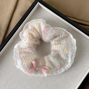 Close-up of a tweed scrunchie with lace trim and pink bow in a white display box