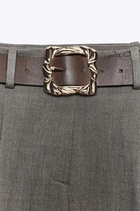 Vue détaillée d'une ceinture en cuir marron avec boucle dorée texturée sur un pantalon gris