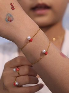 Detalle de una pulsera de cadena dorada con perla blanca y colgante de estrella de mar roja