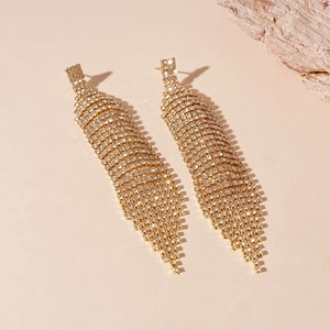 Détail de longues boucles d'oreilles dorées à franges diamantées et pompon cascade
