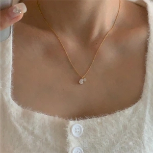 Close-up of golden necklace with round and pear-shaped zircon pendants on white sweater