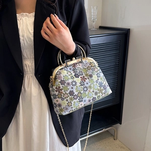 Vintage floral shell bag with gold chain strap held by model in professional setting