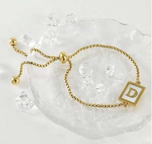 Detail of gold bolo bracelet featuring a square pendant with letter D and shell inlay