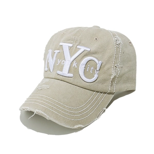 Close-up of NYC embroidery and distressed rip details on beige cotton baseball cap