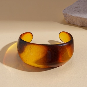 Close-up of a translucent amber acrylic open bangle with warm light refraction