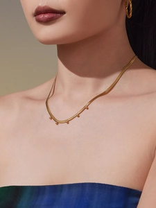 Nahaufnahme einer goldene Schlangenkette mit Perlen und passenden gedrehten Creolen für Damen