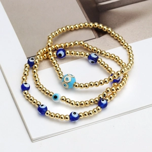 Detailed view of layered gold bead bracelets with blue evil eye charms in a set
