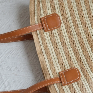 Detail of hand-woven straw texture and brown leather handle with white stitching