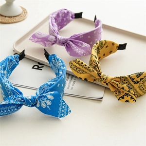 Three paisley print fabric headbands in purple, blue, and yellow with stylish bow knots