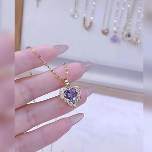 Detailed close-up of a gold heart necklace with blue-purple gradient crystal and zircon wings