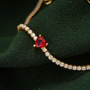 Détail d'un bracelet doré avec zircon rouge en forme de cœur et serti de cristaux