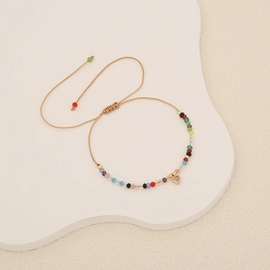 Detailed view of woven crystal bead bracelet with gold heart pendant on wave display