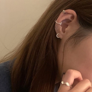 Detailed view of silver heart zircon ear cuffs and wavy ring on a model with soft lighting