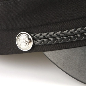 Detail of black military cap featuring silver crest button and braided leather strap