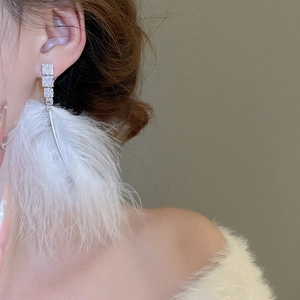 Close-up of elegant white feather tassel earrings with silver zirconia detail on a model