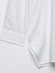 Detailed close-up of white pinstripe fabric texture and stitching on a loose shirt